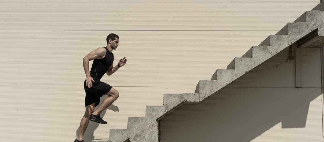Up to top, overcoming challenges. Strong athletic man climbing stairs